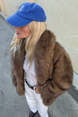 side-view-of-a-model-in-golden-brown-faux-fur-coat-with-wide-collar-styled-with-white-jeans-and-blue-cap